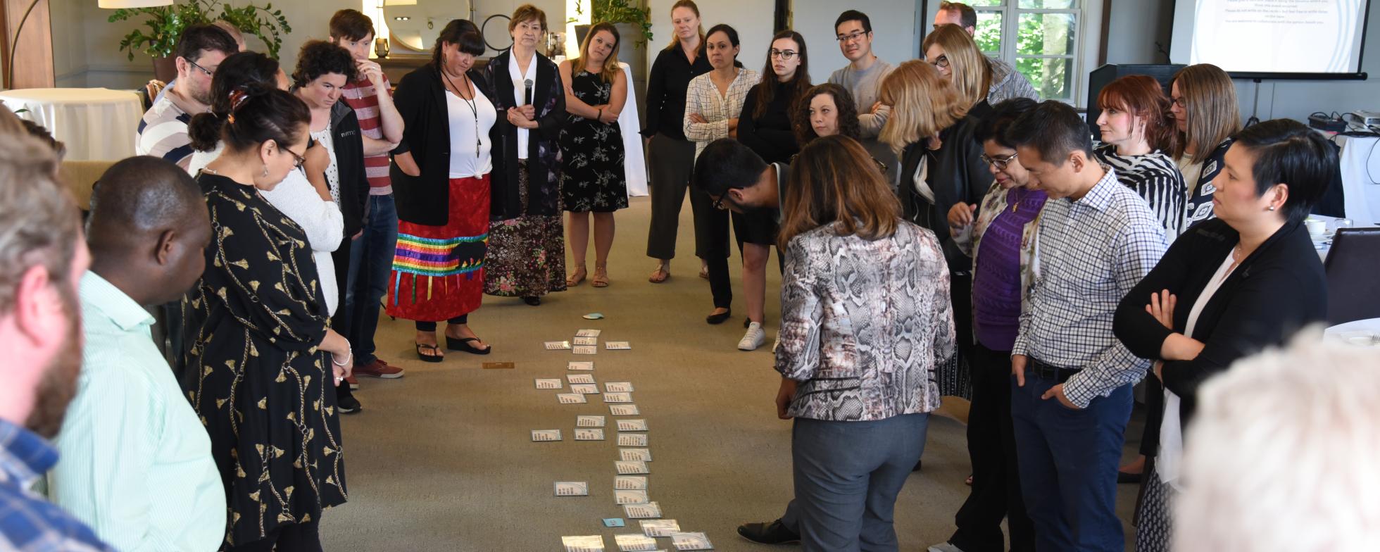 EN: People standing in a circle looking at cards on the floor FR: Les gens se tiennent en cercle en regardant des cartes sur le sol