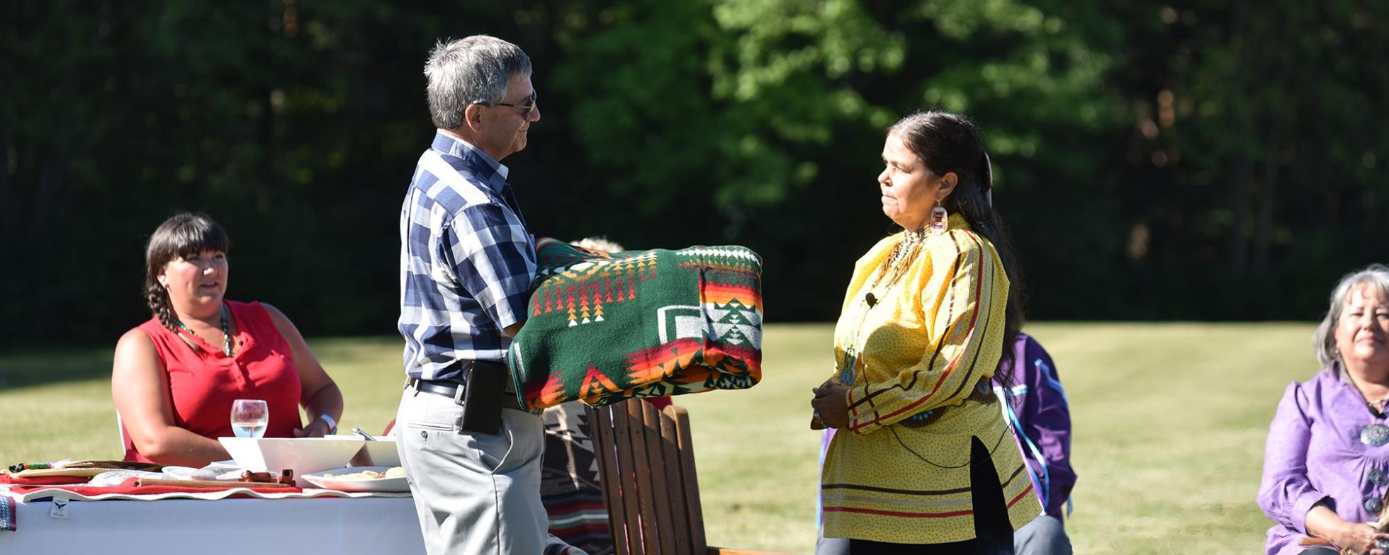 EN: A man is presenting a woman with a patterned blanket FR: Un homme présente une femme avec une couverture à motifs